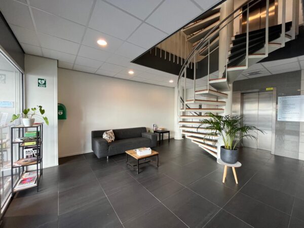 Moderne ontvangstruimte in een kantoorpand in Leidse Rijn met zitbank, wenteltrap, plant en tijdschriftrek.